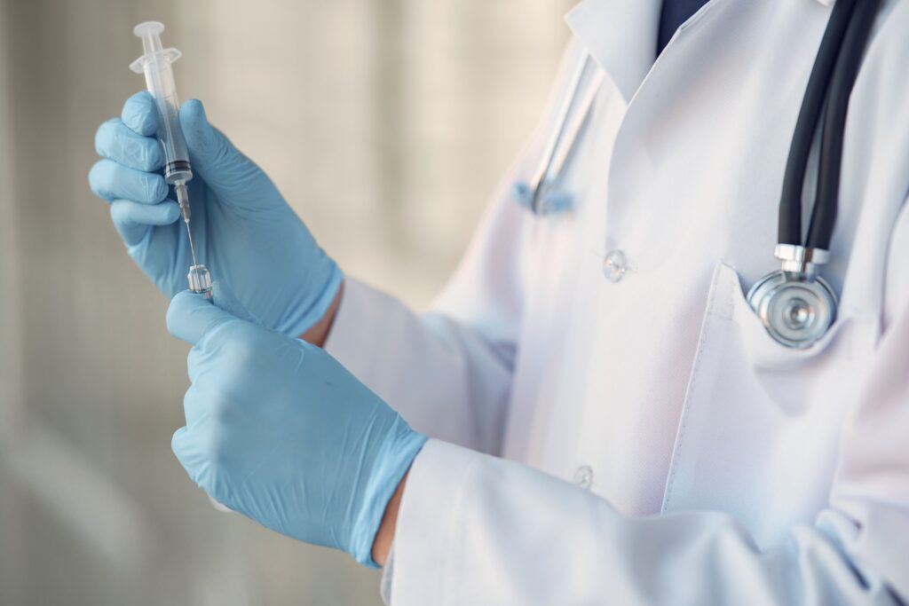Testosterone injection timing: provider in gloves drawing medication from a vial into a syringe