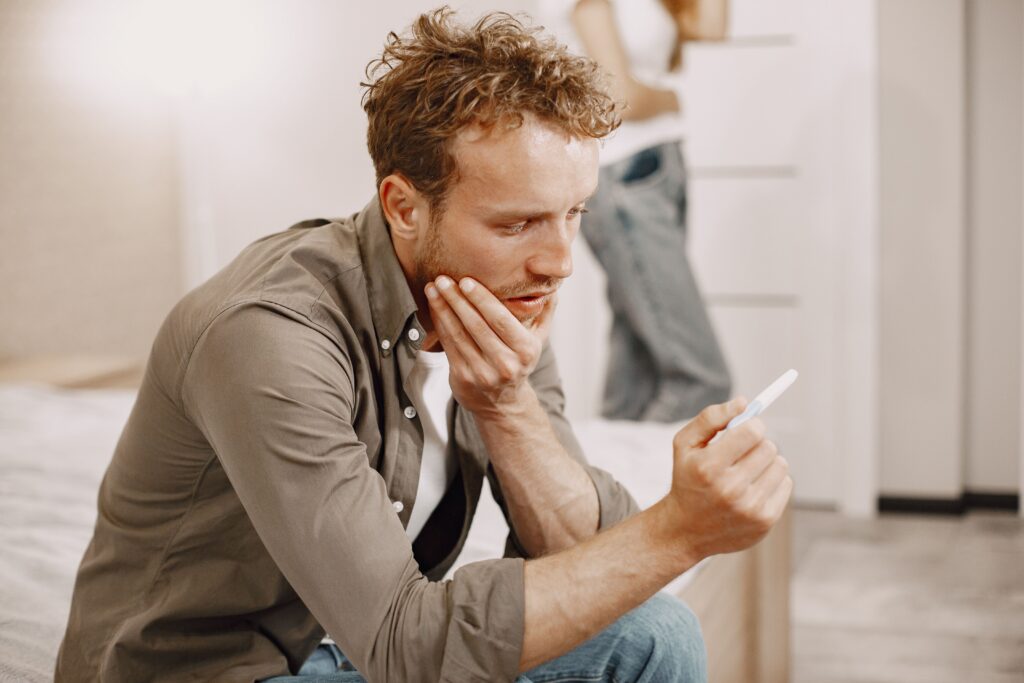 TRT and fertility: worried man looking at a pregnancy test while his partner stands in the background