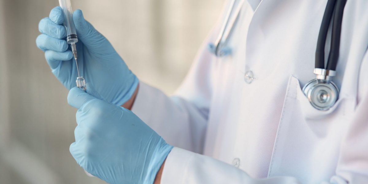 Testosterone injection timing: provider in gloves drawing medication from a vial into a syringe