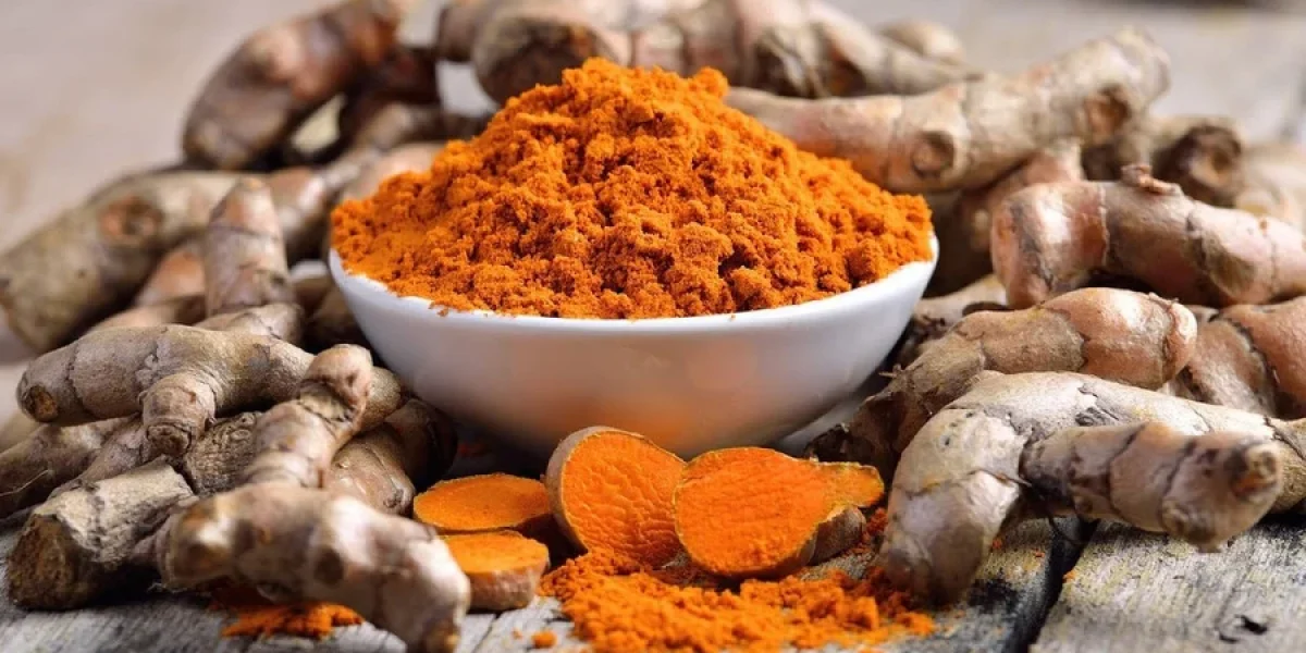 Bowl of ground turmeric powder surrounded by fresh turmeric roots on a rustic wood table